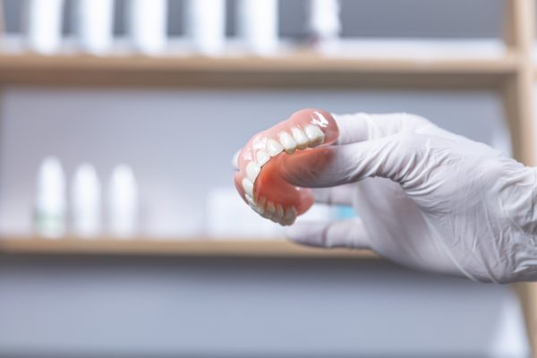 A,Gloved,Hand,Holds,An,Upper,Denture,For,An,Elderly